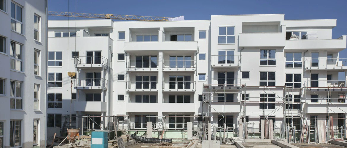 Nowoczesny budynek mieszkalny w trakcie budowy, z rusztowaniami i sprzętem budowlanym na pierwszym planie.